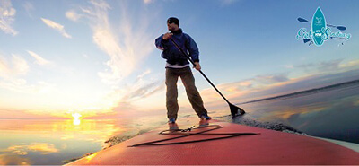 A stand up paddleboarder in front of a sunset